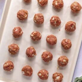 Uncooked meatballs are arranged in rows on a parchment-lined baking sheet, ready to be cooked.