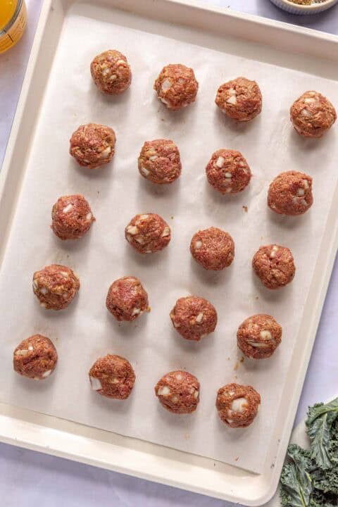 Uncooked meatballs are arranged in rows on a parchment-lined baking sheet, ready to be cooked.