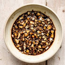 A bowl filled with chopped garlic mixed in a dark soy-based sauce, placed on a light wooden surface.