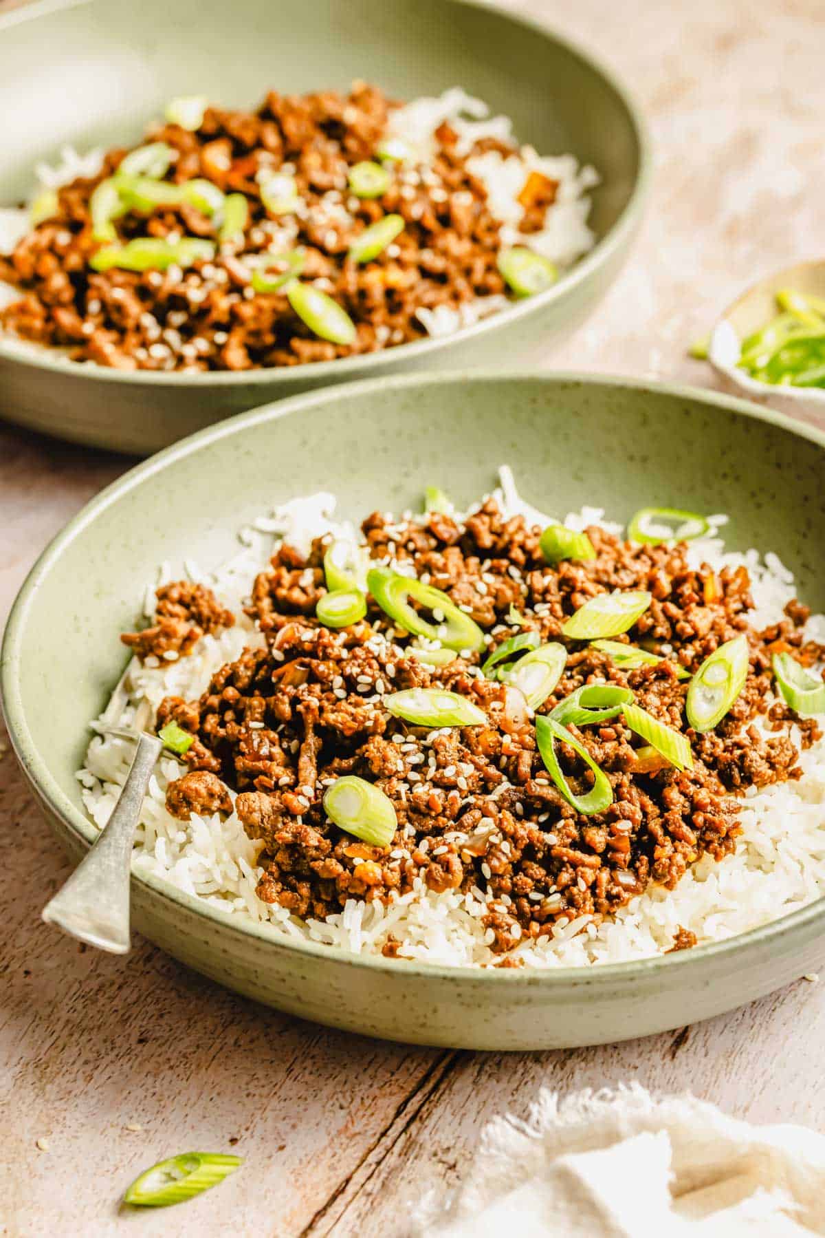 Two bowls of white rice topped with seasoned ground beef, sliced green onions, and sesame seeds, with a fork resting in one bowl.