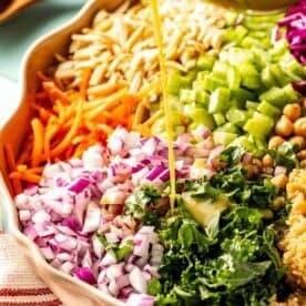 Chopped vegetables, chickpeas, and quinoa in a bowl with salad dressing being poured on top.