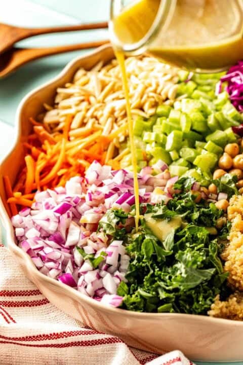 Chopped vegetables, chickpeas, and quinoa in a bowl with salad dressing being poured on top.
