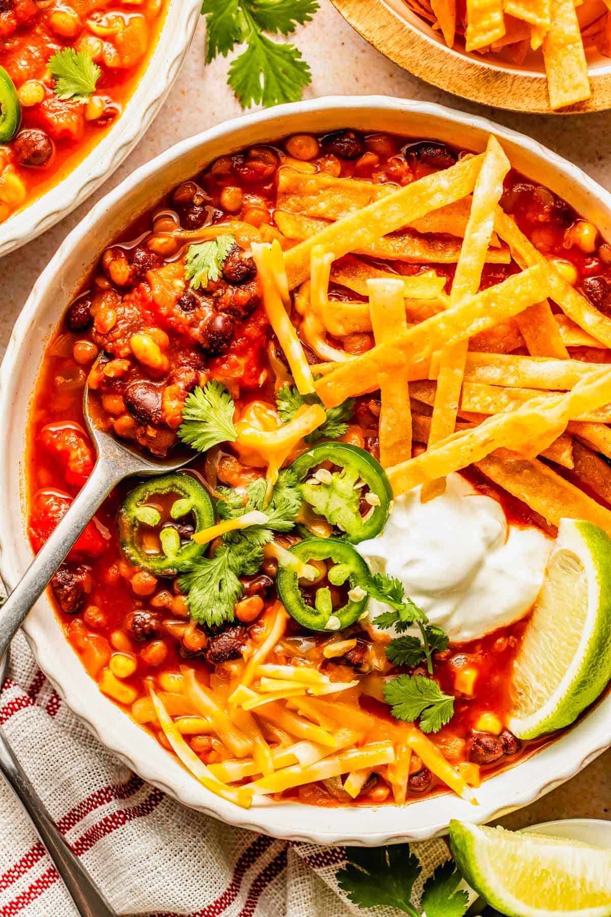 A bowl of tortilla soup topped with tortilla strips, shredded cheese, sour cream, jalapeño slices, and cilantro, with a lime wedge on the side.