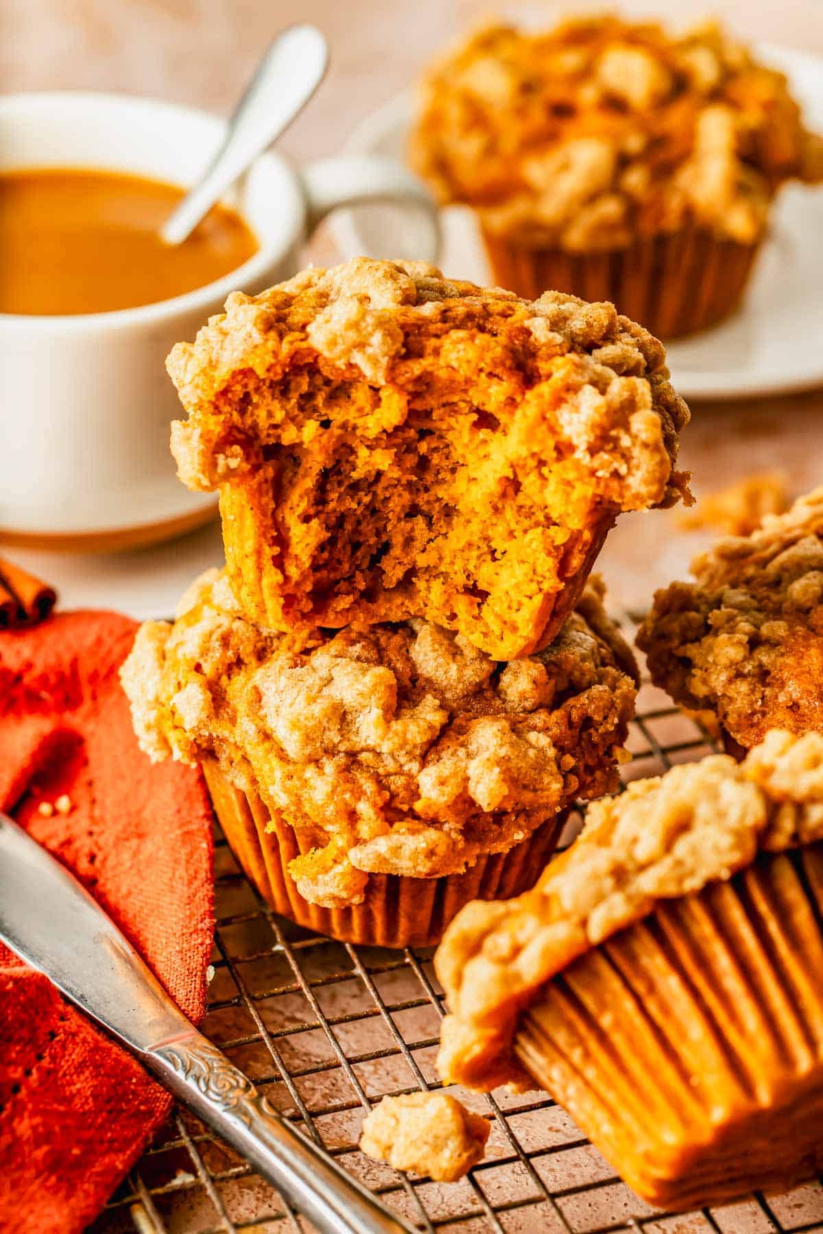 Stacked pumpkin muffins with crumb topping on a wire cooling rack, with a cup of coffee in the background.