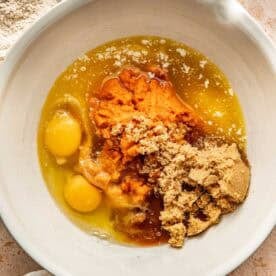 A mixing bowl containing pumpkin puree, two raw eggs, brown sugar, and melted butter.