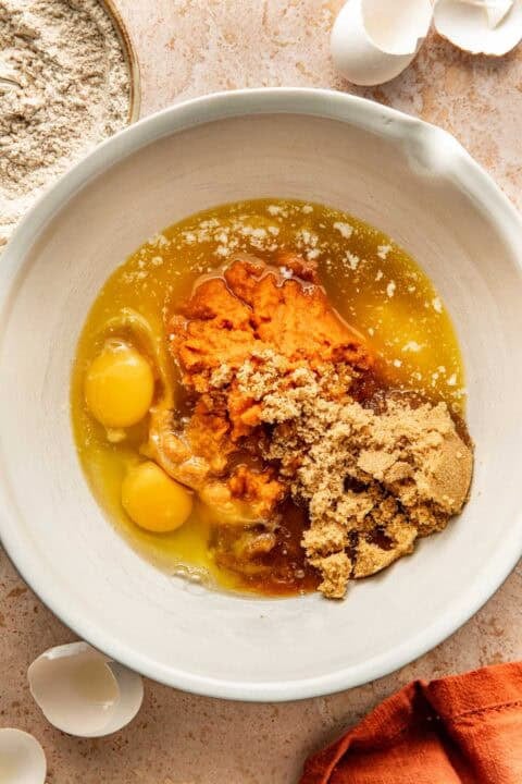 A mixing bowl containing pumpkin puree, two raw eggs, brown sugar, and melted butter.