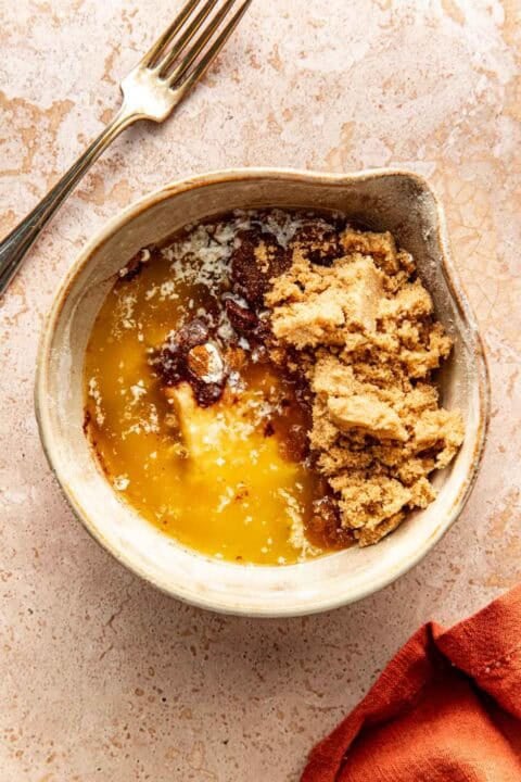 A bowl containing melted butter, brown sugar, and spices, with a fork resting nearby.