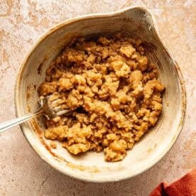 A metal fork in a bowl containing a crumbly brown sugar mixture.