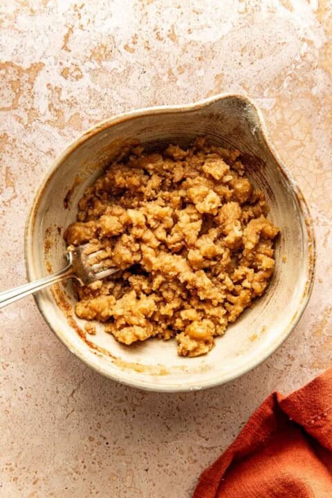 A metal fork in a bowl containing a crumbly brown sugar mixture.