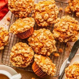 Pumpkin crumb muffins cooling on a wire rack next to two cups of coffee.