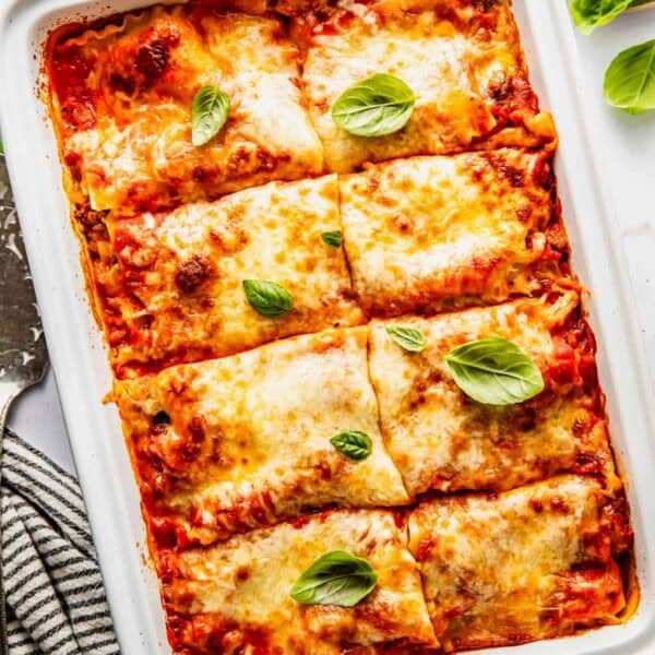 A rectangular baking dish filled with six square portions of baked lasagna topped with melted cheese and fresh basil leaves.